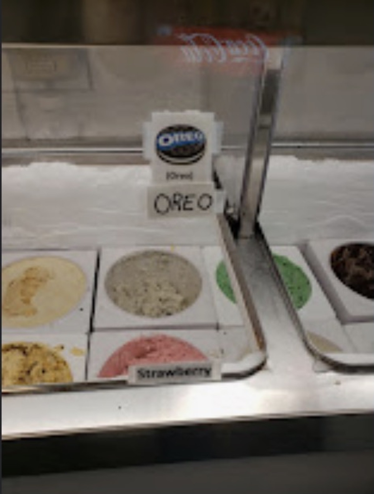 Open tubs of Oreo, strawberry, mint and chocolate ice cream behind the freezer glass
