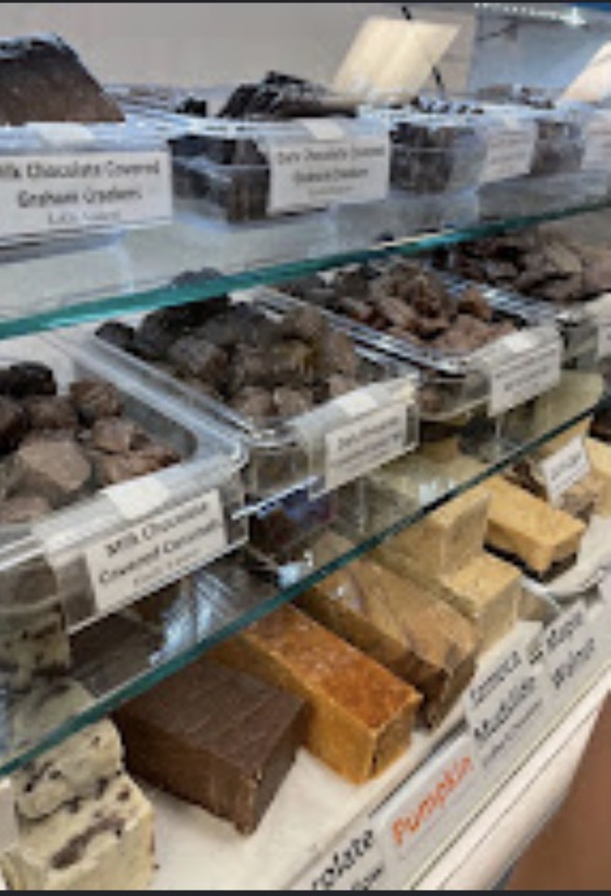 Glass case of fudge slabs and chocolate covered graham crackers with handwritten labels