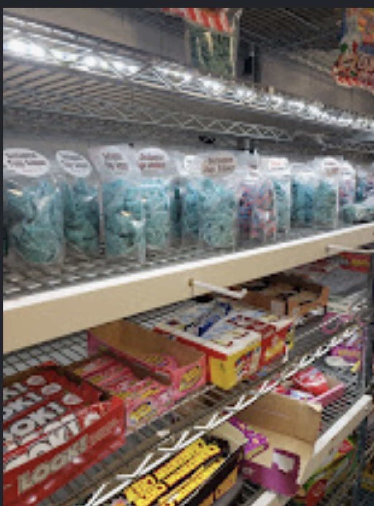 Row of labeled bags of blue cotton candy on a lit shelf